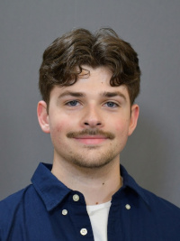 A headshot of Matt smiling in a navy oxford shirt against a gray background.